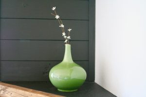 vintage green vase on a mantel with white faux flowers in it