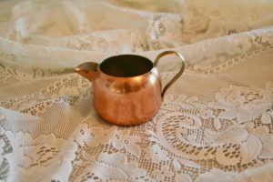 copper creamer displayed on a lace cloth