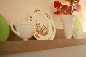 a vintage floral plate displayed on a picture rail with milk glass
