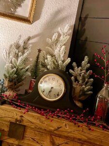 a mantel clock surrounded by flocked Christmas trees