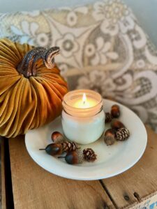 a handmade soy wax fall candle lit and sitting on a vintage plate surrounded by acorns