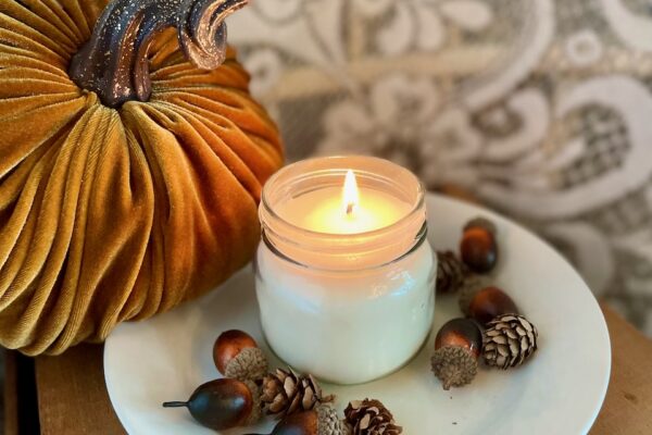 a handmade soy wax fall candle lit and sitting on a vintage plate surrounded by acorns