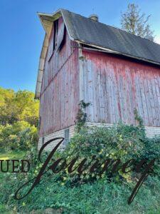 a large old, red barn out in the country surrounded by woods