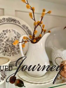 a vintage ironstone pitcher styled for Thanksgiving in a hutch with gold stems