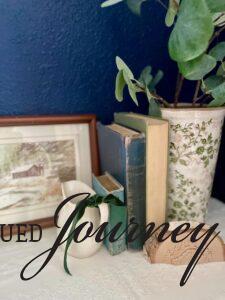 a Christmas vignette styled on a dresser with vintage books, winter art, and ironstone