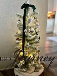 a small flocked tree with shiny brite ornaments styled in an entryway