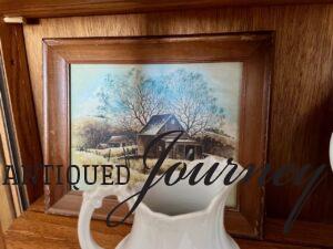 a thrifted barn art print styled inside a curved cabinet