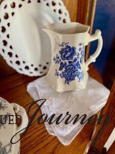 a vintage hanky styled with a blue and white pitcher inside a glass curio cabinet