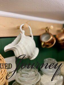 a vintage ironstone creamer hanging on a peg rack for vintage kitchen decor