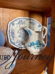 a vintage blue and white pitcher in a curved curio cabinet
