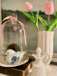 Spring bathroom vignette with a vintage cloche display, milk glass, ironstone, and a ceramic bunny