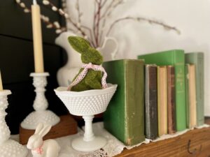 Thrifted spring mantel display with ironstone, milk glass, moss, ceramic bunnies, and faux taper candles