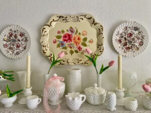Vintage milk glass wall shelf styled for spring with pink lace ribbon, faux tulips, and a toile tray