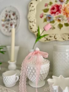 Simple spring shelf styling with vintage milk glass, a toile tray, pink lace ribbon, and faux pink tulips