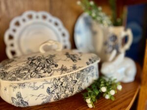 top shelf of a wood curio cabinet styled with vintage blue and white pitchers and florals