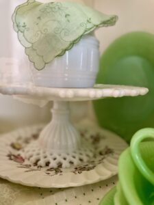 A vintage milk glass cake stand styled in a hutch