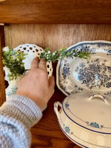 styling faux greenery in an antique curio cabinet for spring
