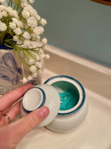Vintage lidded jar holding floss picks on a bathroom countertop