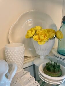 Full view of a vintage and thrifted cottage-style summer hutch with blue glass, milk glass, and faux florals