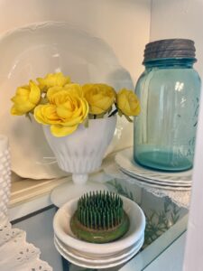 Blue vintage ball jars and milk glass styled on a hutch shelf with faux yellow flowers for summer cottage decor