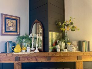 A fully styled summer fireplace mantel with vintage enamelware, ferns, and milk glass