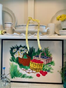 Close up of vintage needlework art styled into a summer hutch vignette with ironstone and linen